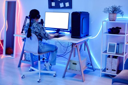 Foto de Retrato de larga duración de la joven adolescente jugando videojuegos por la noche en la habitación con iluminación de neón azul, espacio de copia - Imagen libre de derechos