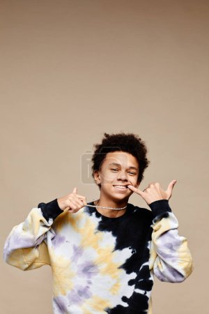 Photo for Vertical portrait of black teenage boy wearing tie dye shirt over neutral beige background, copy space - Royalty Free Image