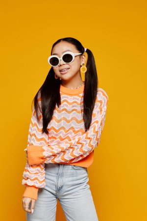 Photo for Vertical portrait of teenage Asian girl wearing white sunglasses over vibrant yellow background - Royalty Free Image