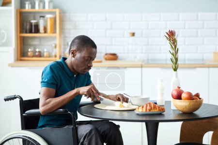 Foto de Retrato de vista lateral del hombre negro con discapacidad disfrutando de un desayuno saludable en la elegante cocina casera, espacio para copiar - Imagen libre de derechos