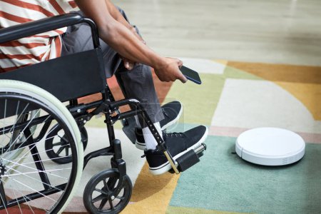 Foto de Primer plano hombre con discapacidad utilizando robot aspiradora y la tecnología del hogar inteligente, espacio de copia - Imagen libre de derechos