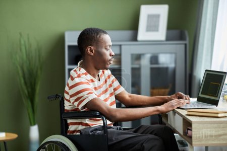 Photo for Side view portrait of African American man with disability using laptop while working from home - Royalty Free Image