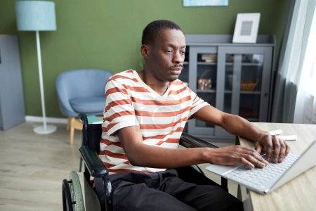 Foto de Retrato de un hombre afroamericano adulto con discapacidad usando una computadora portátil mientras trabaja desde casa - Imagen libre de derechos