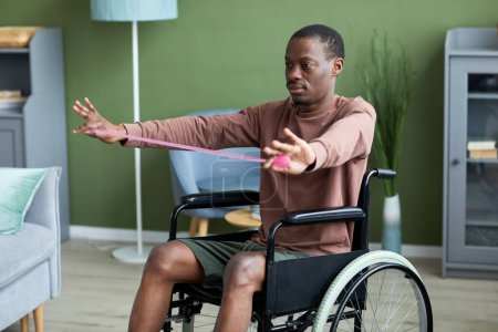 Foto de Retrato de un hombre afroamericano adulto con discapacidad que hace ejercicio en casa usando elásticos - Imagen libre de derechos