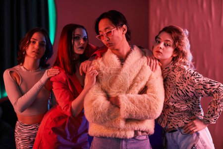 Photo for Group of young girls posing with extravagant Asian man in nightclub lit by pink neon light - Royalty Free Image