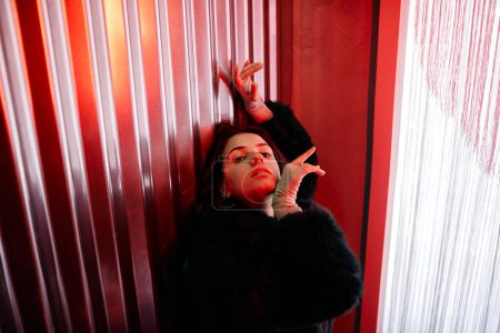 Foto de Retrato de alto ángulo de sensual mujer joven bailando estilo de moda en luz de neón rojo y mirando a la cámara, espacio de copia - Imagen libre de derechos