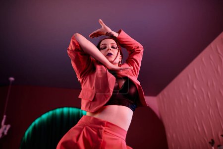 Foto de Retrato en ángulo bajo de una sensual joven bailando estilo de moda en luz de neón rosa con enfoque en los movimientos de las manos - Imagen libre de derechos
