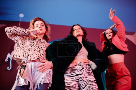 Photo for Low angle portrait of three girls clubbing and dancing vogue style in red neon light - Royalty Free Image