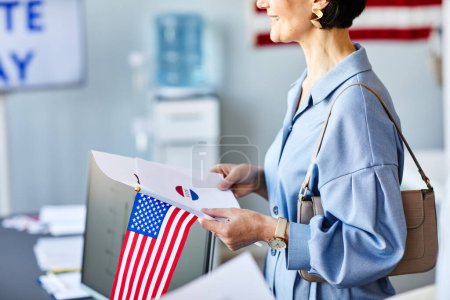 Foto de Vista lateral recortada de la sonriente mujer que sostiene la boleta electoral y la bandera estadounidense el día de las elecciones - Imagen libre de derechos