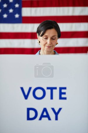 Téléchargez les photos : Plan vertical graphique de la femme adulte dans l'isoloir avec drapeau américain en arrière-plan - en image libre de droit
