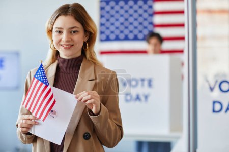 Foto de Retrato en la cintura de una joven sonriente sosteniendo la bandera estadounidense en el centro de votación el día de las elecciones, espacio para copiar - Imagen libre de derechos