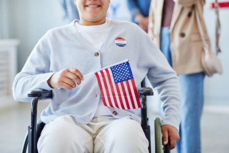 Téléchargez les photos : Gros plan de la jeune femme en fauteuil roulant tenant le drapeau américain après avoir voté le jour du scrutin, espace de copie - en image libre de droit