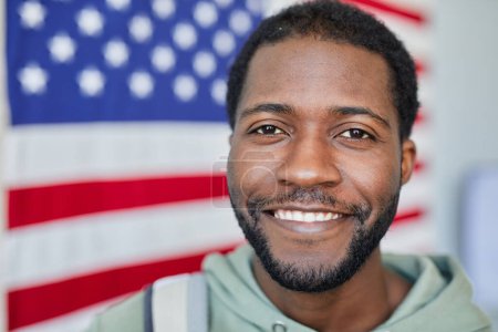 Téléchargez les photos : Portrait rapproché d'un homme noir souriant regardant la caméra contre le drapeau américain en arrière-plan, espace de copie - en image libre de droit