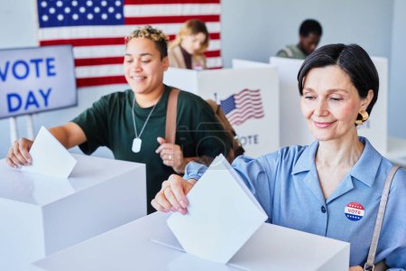 Téléchargez les photos : Portrait de deux Américaines souriantes votant et mettant des bulletins de vote dans des bacs le jour du scrutin, espace de copie - en image libre de droit