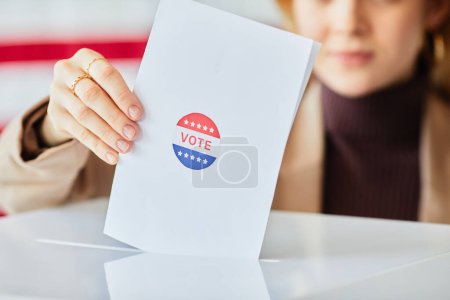 Téléchargez les photos : Gros plan de la jeune femme qui met son bulletin de vote dans la cellule de vote sur fond de drapeau américain, espace de copie - en image libre de droit