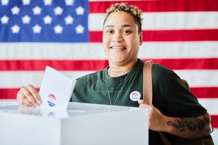Téléchargez les photos : Portrait de femme afro-américaine souriante mettant le bulletin de vote dans la poubelle sur fond de bannière des États-Unis, espace de copie - en image libre de droit