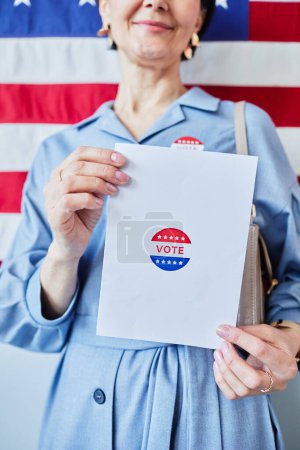 Téléchargez les photos : Gros plan de la femme tenant un bulletin de vote contre la bannière des États-Unis en arrière-plan - en image libre de droit