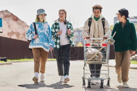 Photo for Group of teens walking along the street and carrying shopping cart with their stuffs - Royalty Free Image