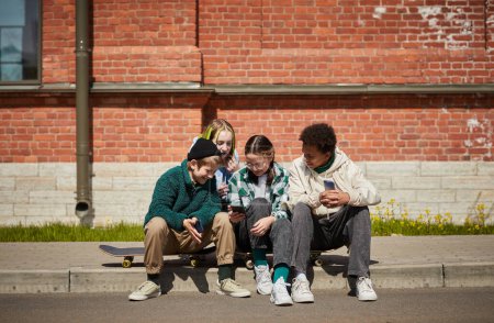 Photo for Group of teenagers sitting on skateboards outdoors and having fun of watching video online on their smartphones - Royalty Free Image