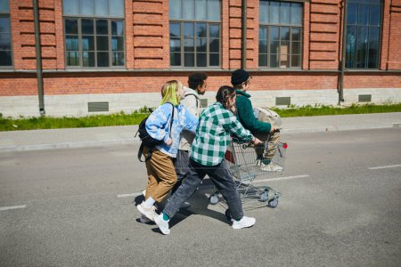 Téléchargez les photos : Groupe d'adolescents jouant à l'extérieur ensemble, ils se chevauchent sur un chariot le long de la rue - en image libre de droit