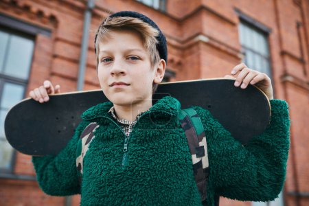 Photo for Portrait of teenage boy holding skateboard looking at camera while standing outdoors in the city - Royalty Free Image