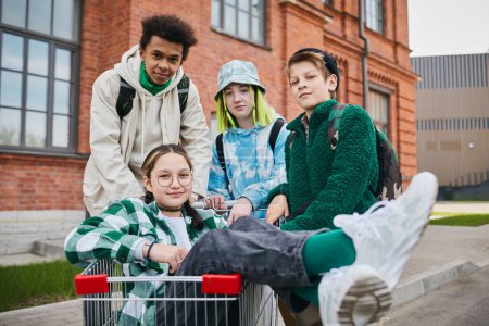 Photo for Portrait of multiethnic teenagers looking at camera while having fun outdoors with shopping cart - Royalty Free Image