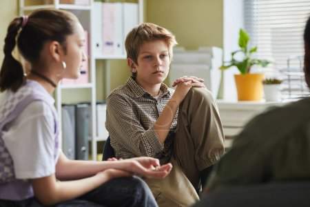 Enfant difficile assis sur une chaise et écoutant d'autres enfants pendant une séance de psychothérapie