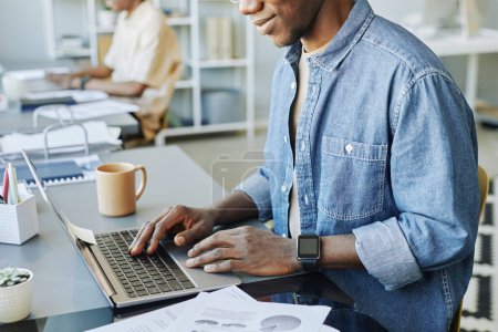 Photo for Cropped shot of young man typing at laptop keyboard in coworking space with people in background - Royalty Free Image