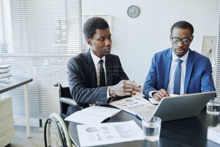 Téléchargez les photos : Portrait de l'homme afro-américain handicapé en réunion d'affaires avec un partenaire discutant de statistiques financières, espace de copie - en image libre de droit