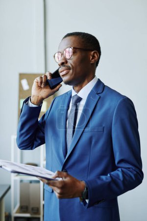 Foto de Retrato vertical del hombre de negocios afroamericano profesional hablando por teléfono en la oficina - Imagen libre de derechos
