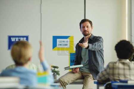 Téléchargez les photos : Portrait d'un enseignant barbu posant des questions en classe avec des enfants levant la main, espace de copie - en image libre de droit