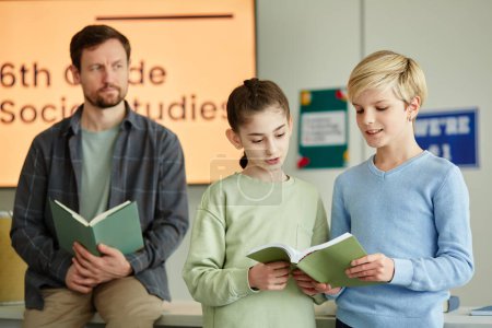 Foto de Retrato de la cintura hacia arriba de dos niños respondiendo preguntas en la escuela frente al aula y sosteniendo el libro - Imagen libre de derechos
