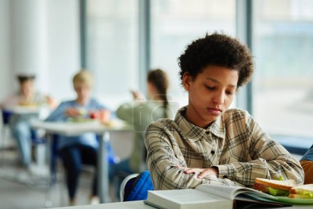 Téléchargez les photos : Portrait de jeune fille noire lisant le livre à la pause déjeuner dans la cantine scolaire, espace de copie - en image libre de droit