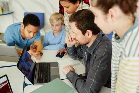 Photo for High angle portrait of male teacher with diverse group of kids using laptop in school - Royalty Free Image