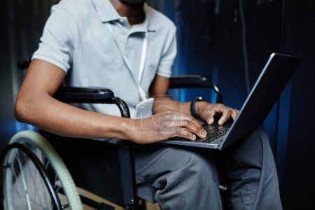 Foto de Recortado disparo de hombre negro con discapacidad utilizando el ordenador portátil en la sala de servidores mientras trabajaba como técnico de TI - Imagen libre de derechos