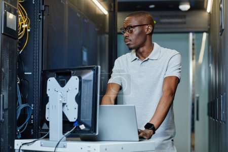 Photo for Portrait of African American man connecting laptop to server in server room and setting up internet network, copy space - Royalty Free Image