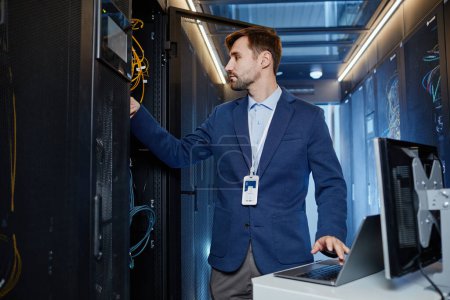 Photo for Waist up portrait of young man wearing blazer setting up internet network in server room - Royalty Free Image