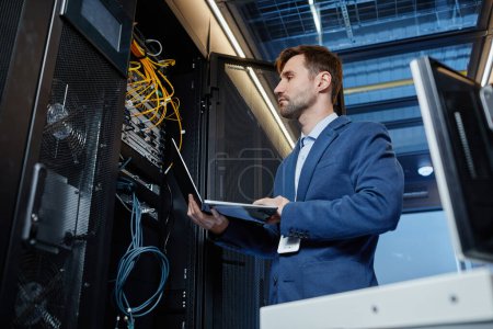 Foto de Retrato de ángulo bajo del ingeniero de TI que sostiene el ordenador portátil mientras configura la red de Internet en la sala de servidores - Imagen libre de derechos