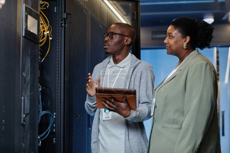 Photo for Waist up portrait of black IT engineer with female assistant in server room inspecting network systems - Royalty Free Image
