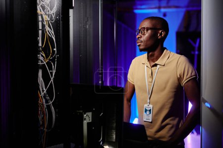 Photo for Side view portrait of adult African American man working in server room and setting up data network - Royalty Free Image