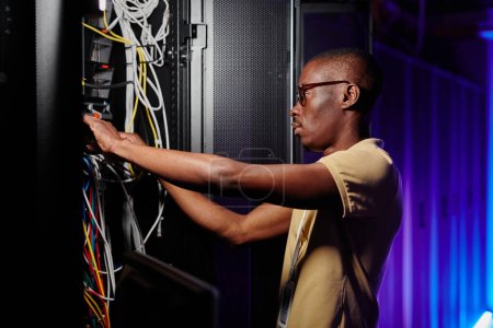 Seitenansicht Porträt eines erwachsenen afroamerikanischen Mannes, der Server repariert und ein Datennetzwerk einrichtet
