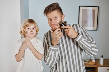 Photo for Waist up portrait of handsome young father teaching son shaving and looking at camera - Royalty Free Image