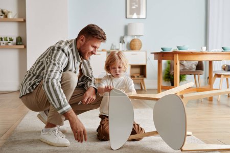 Téléchargez les photos : Portrait complet de père et fils heureux assemblant des meubles ensemble dans une maison chaleureuse et confortable, espace de copie - en image libre de droit