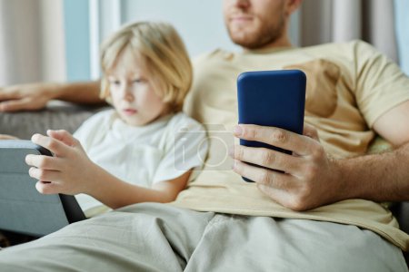 Téléchargez les photos : Gros plan du père tenant smartphone avec petit garçon en utilisant une tablette en arrière-plan, espace de copie - en image libre de droit