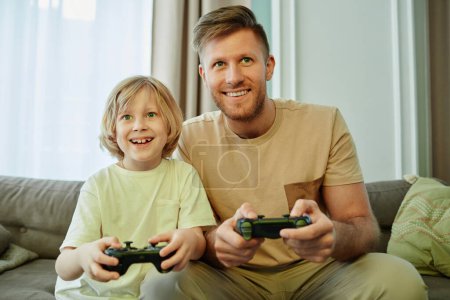Photo for Front view portrait of father and son playing video games together and smiling happily - Royalty Free Image