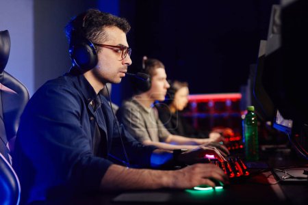 Foto de Retrato de vista lateral de un joven jugando videojuegos con un equipo de ciberdeporte en segundo plano, espacio para copiar - Imagen libre de derechos