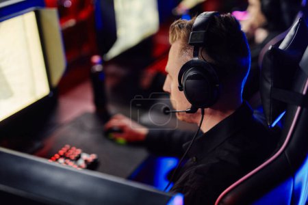 Photo for Side view portrait of adult man playing video games on PC and wearing headset mic with cybersport team - Royalty Free Image