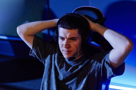 Photo for Portrait of man playing video games in cyber sport club lit by blue neon and wearing headset, copy space - Royalty Free Image