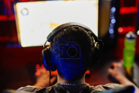 Photo for Back view at man playing video games in dark, focus on head with headphones, copy space - Royalty Free Image