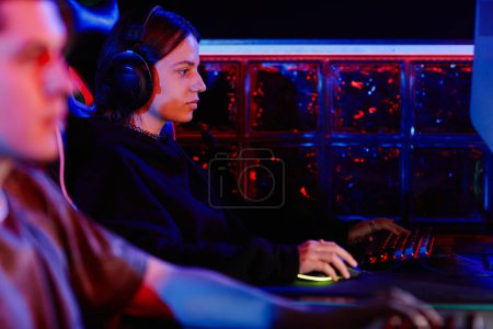 Photo for Side view portrait of young woman playing video games with cyber sports team in neon light, copy space - Royalty Free Image